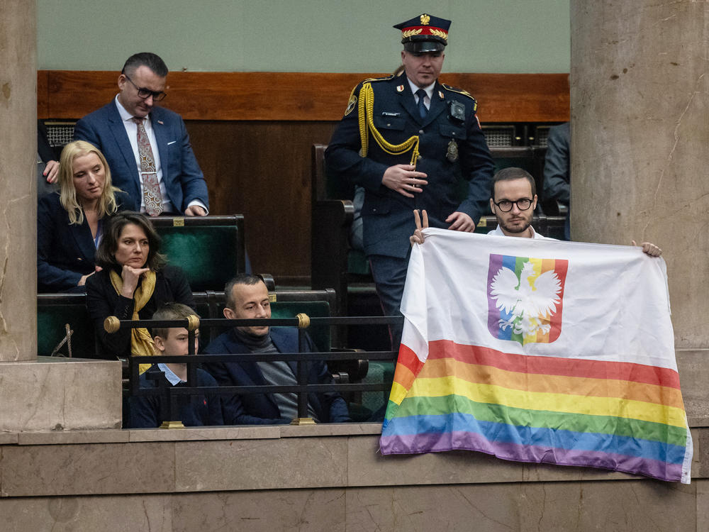 Polish filmmaker and LGBTQ+ activist Bart Staszewski holds a rainbow Pride-themed flag on the gallery of the Polish Parliament as designated Polish Prime Minister Donald Tusk gives a speech to present his program to lawmakers in Warsaw on Dec. 12.