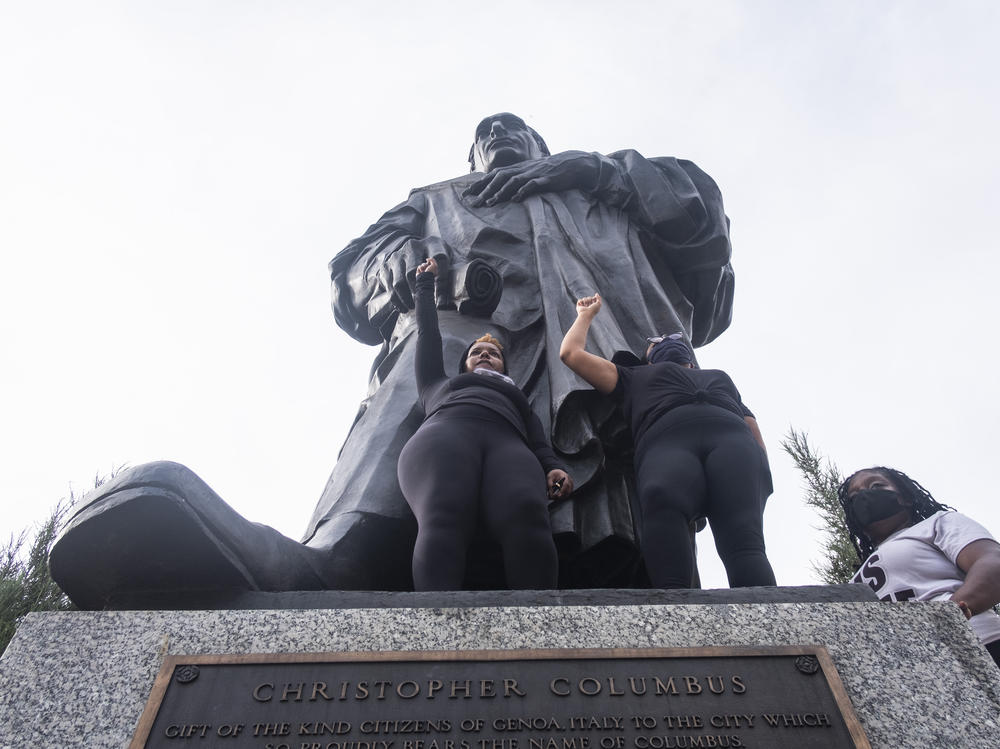 Protesters hold their fists in the air at the base of the Christopher Columbus Statue at Columbus City Hall during a protest organized against police brutality and the Columbus statue on June 27, 2020.