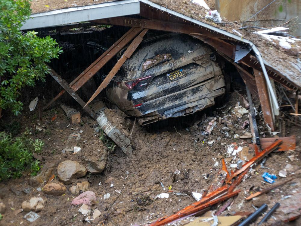 A car remains in the wreckage after a house and garage were abruptly destroyed by a landslide as an atmospheric river storm inundates the Hollywood Hills area of Los Angeles on Feb. 6, 2024. A spate of natural disasters is helping lead to soaring insurance premiums across the country.