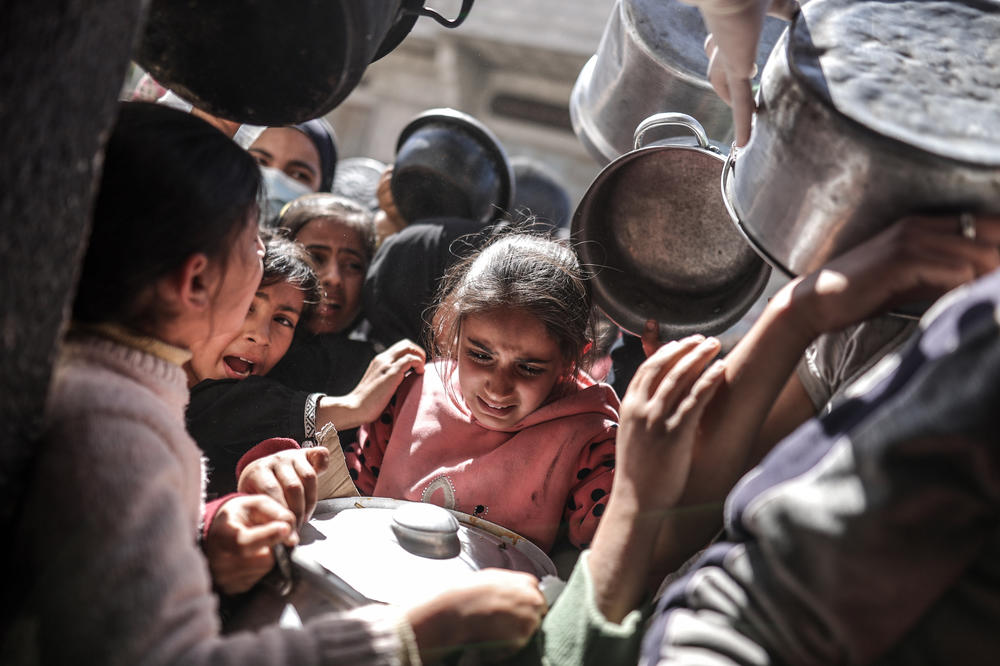 Palestinians with empty pots receive food distributed by charity, in Deir al-Balah, central Gaza, on Thursday. Gaza faces a worsening hunger crisis amid a blockade and ongoing Israeli offensive.