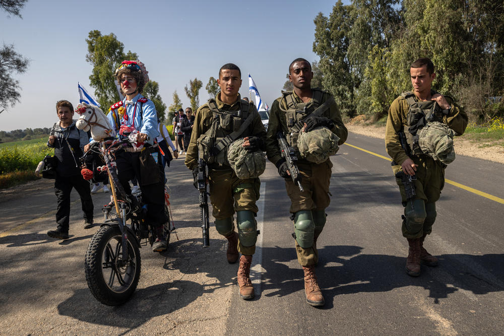 An Israeli activist dressed as a clown rides an electric bike alongside Israeli soldiers accompanying families of the hostages and supporters near the start of the four-day march to Jerusalem on Feb. 28. The activist, who goes by the name 