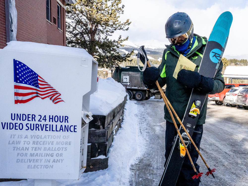 Bob Christie carrying his skis on the way to the slopes in Breckenridge, Colo., drops off his ballot on March 5, 2024.