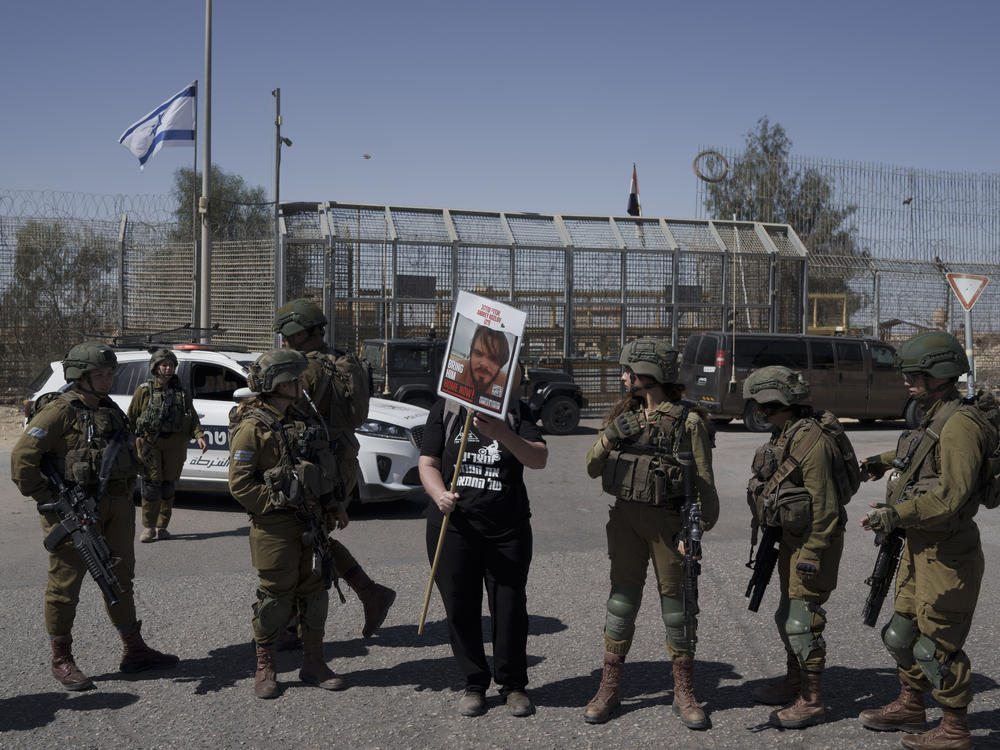 A woman holds up a sign for a hostage held captive by Hamas in Gaza as she stands next to Israeli soldiers at Israel's Nitzana border crossing with Egypt in southern Israel on Tuesday, March 5, where the group protests the delivery of humanitarian aid to Gaza until all of the hostages being held by Hamas militants have been released.