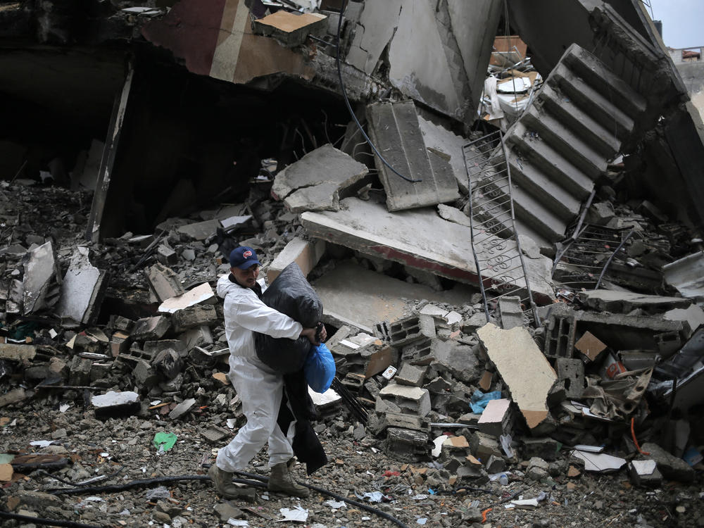 A Palestinian carries some of his belongings on Thursday, March 7, as he walks by buildings destroyed in Israeli bombing after returning briefly to Khan Younis, in southern Gaza, to check on what remains of his home.