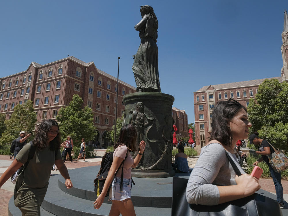 Students walk by the statue of Hecuba, the legendary Queen of Troy, with a quote by William Shakespeare — spelled 