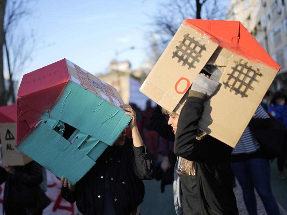 Two young women wear cardboard houses over their heads during a demonstration protesting Portugal's housing crisis, in Lisbon, Jan. 27, 2024.