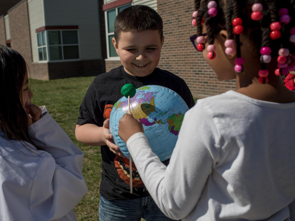 Second graders Hanah Sung, Izaac Stuck and Amaurie Robinson simulate an eclipse by casting a shadow with a play dough moon on an inflatable globe. Their teacher, Natasha Cummings, directs them to aim the shadow over the spot on the globe where Indianapolis would be.