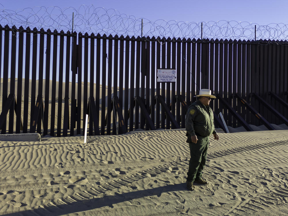 A U.S. Border Patrol agent stands near the border fence, which stretches through the Imperial Sand Dunes in California.