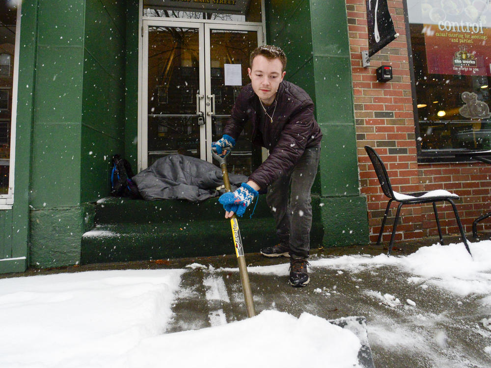 Mikey Reynolds, an employee at The Works on Main Street in Brattleboro, Vt., shovels the sidewalk in front of the restaurant as a person who is facing homelessness sleeps in a door entryway while seeking refuge from the snow storm on Saturday, March 23, 2024.