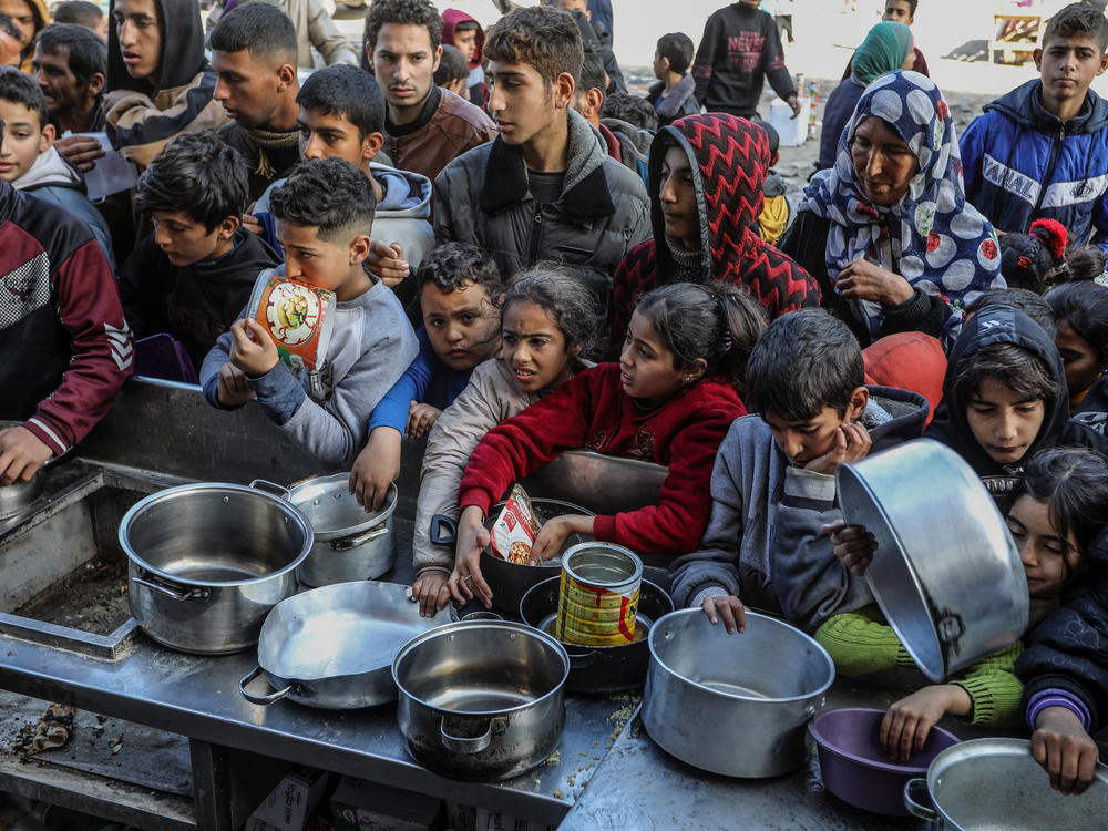 Palestinian people with empty bowls wait for food at a donation point in Rafah. A report out this week shows widespread hunger and malnutrition in Gaza but stopped short of declaring it a 