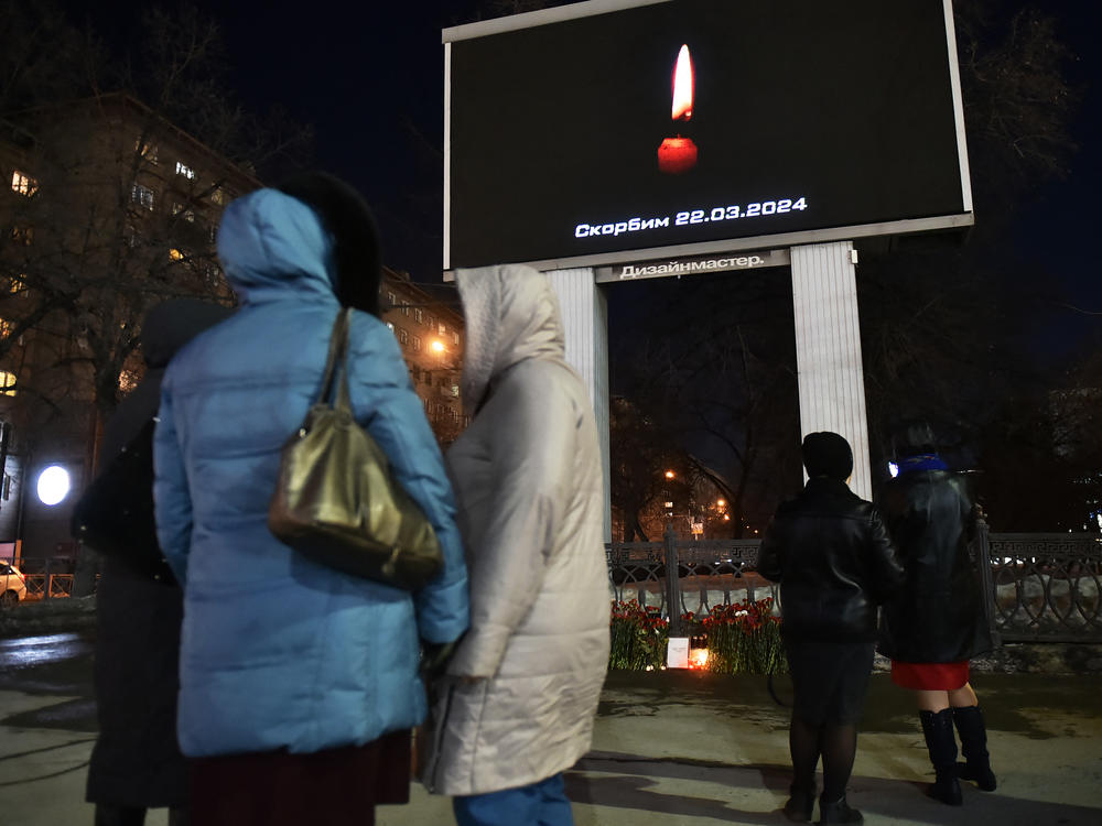 People stand next to an advertising screen displaying an image of a lit candle and the slogan 