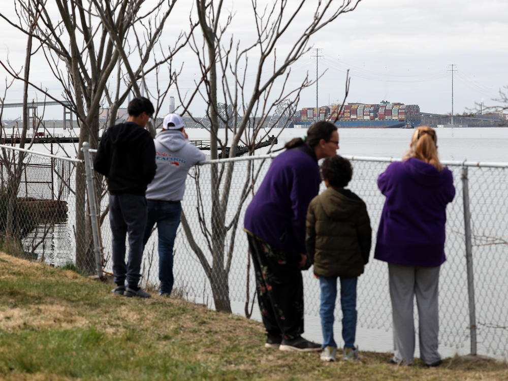 Residents look on after a cargo ship ran into and collapsed the Francis Scott Key Bridge on March 26, 2024 in Baltimore. Conspiracy theorists online quickly spread narratives to millions online that the accident was part of a nefarious scheme.