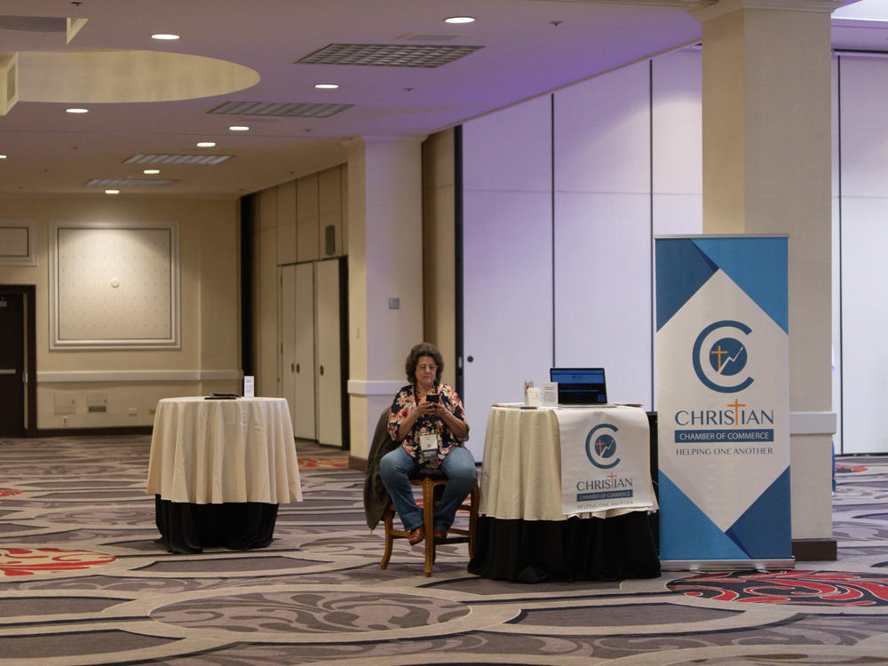 A woman sits at the Christian Chamber of Commerce booth at the RePlatform conference.