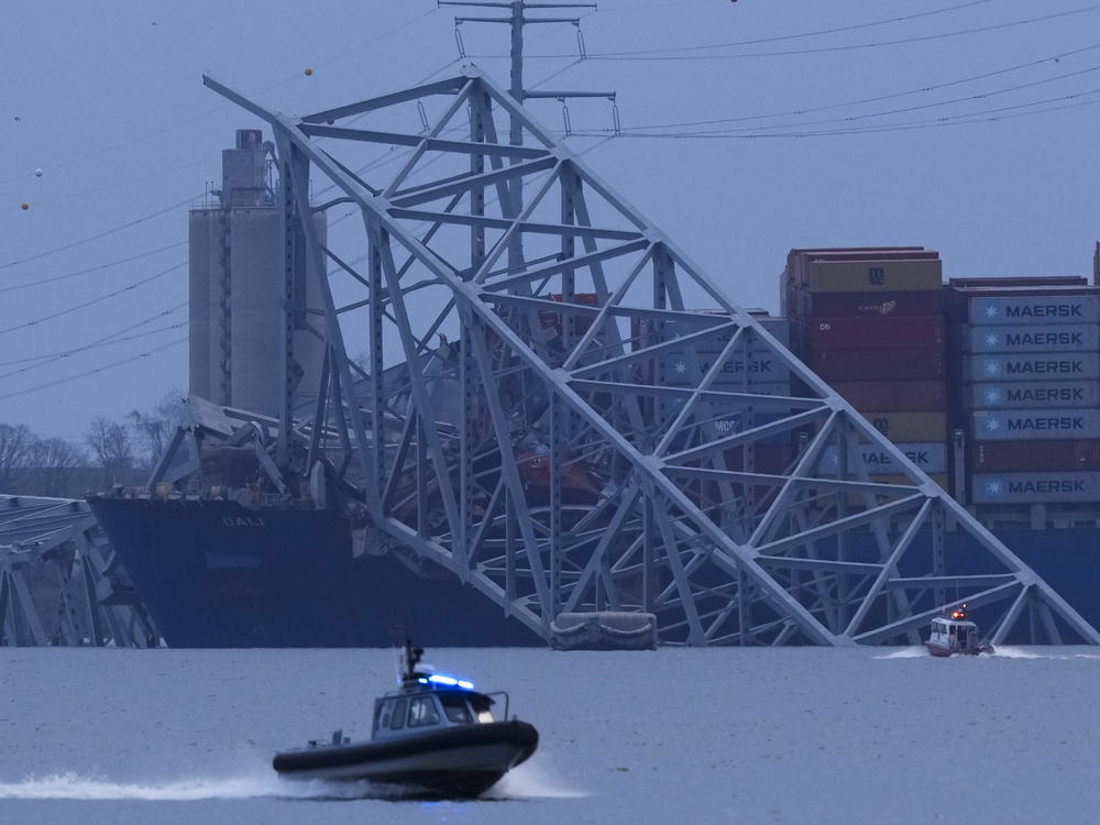 A container ship rests against wreckage of the Francis Scott Key Bridge as night falls on Tuesday, as seen from Sparrows Point, Md.