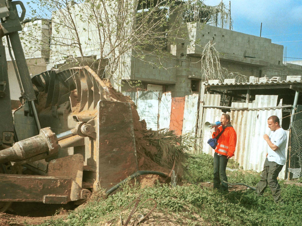 American activist Rachel Corrie (left), 23, stands between an Israeli bulldozer and a Palestinian house on March 16, 2003, in Rafah in the Gaza Strip. Corrie was run over and killed by an Israeli bulldozer as she protested the demolition of Palestinian houses.