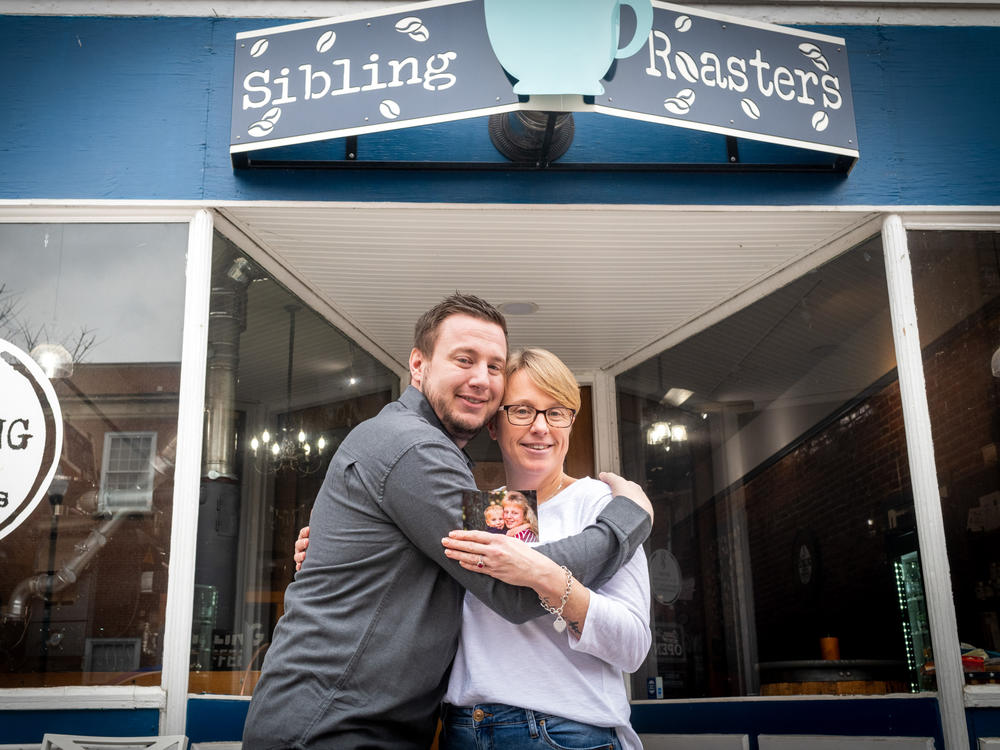 Sibling Coffee Roasters owner Libby Powell poses with her brother, Benjamin Withem, outside her West Virginia coffee shop. In her hand is an early photo of the pair — one they are trying to re-create.