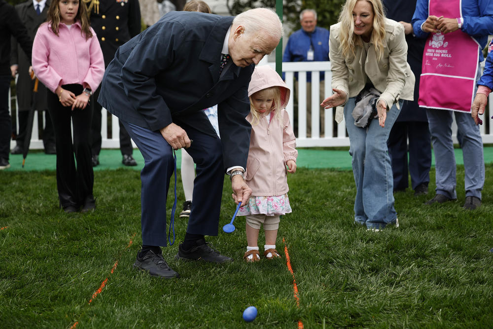 President Joe Biden helps a young guest roll her hard-boiled egg down at the White House Easter Egg Roll.