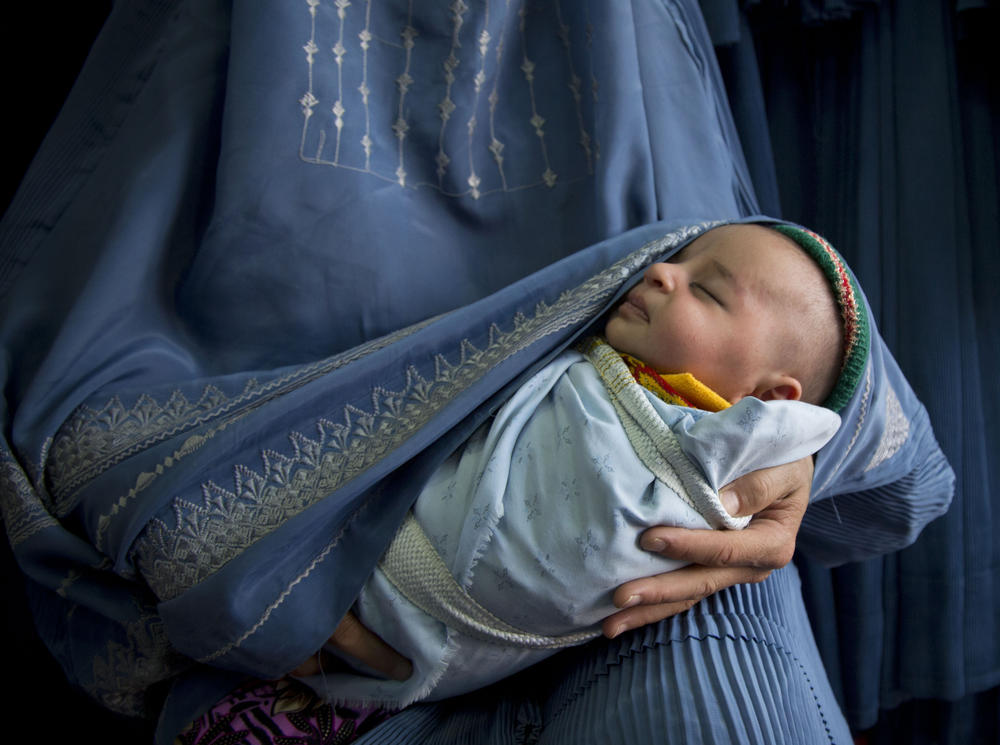 An Afghan woman holds her newborn baby wrapped in her burqa as she waits to get in line to try on a new burqa in a shop in Kabul, Afghanistan, April 11, 2013.
