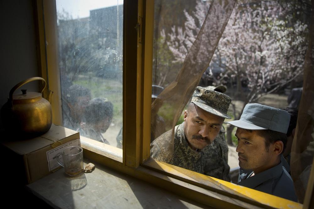 An Afghan soldier, left, and a policeman peek through a window as they queue with others to get their registration cards on the last day of voter registration for presidential elections, outside a school in Kabul, Afghanistan, April 1, 2014. Niedringhaus was killed on April 4, 2014.