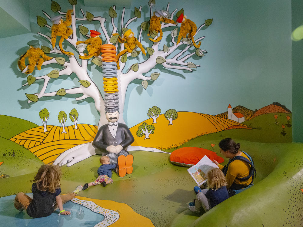 Lindsey Anderson sits down to read <em>Caps for Sale</em> by Esphyr Slobodkina to her children Orion, 6, Arthur, 4, and Thora Hoke, 1, inside the exhibit inspired by the book inside The Rabbit hOle, an immersive museum dedicated to children's literature, in North Kansas City, Mo.