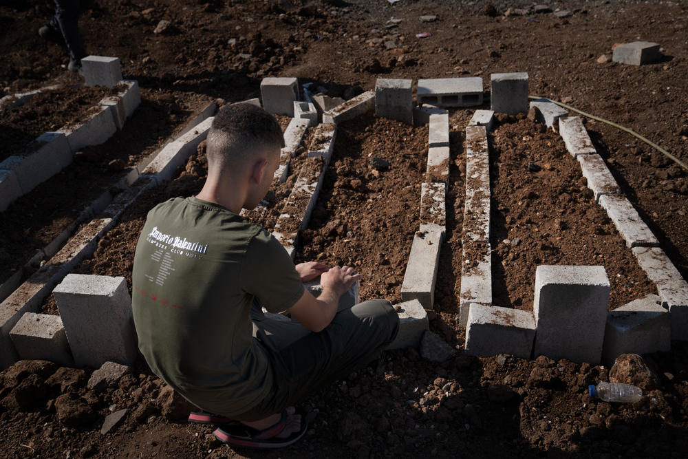 A young man sits by the fresh graves of two teenagers and a 20-year-old killed in an Israeli drone strike in Jenin, in the occupied West Bank.
