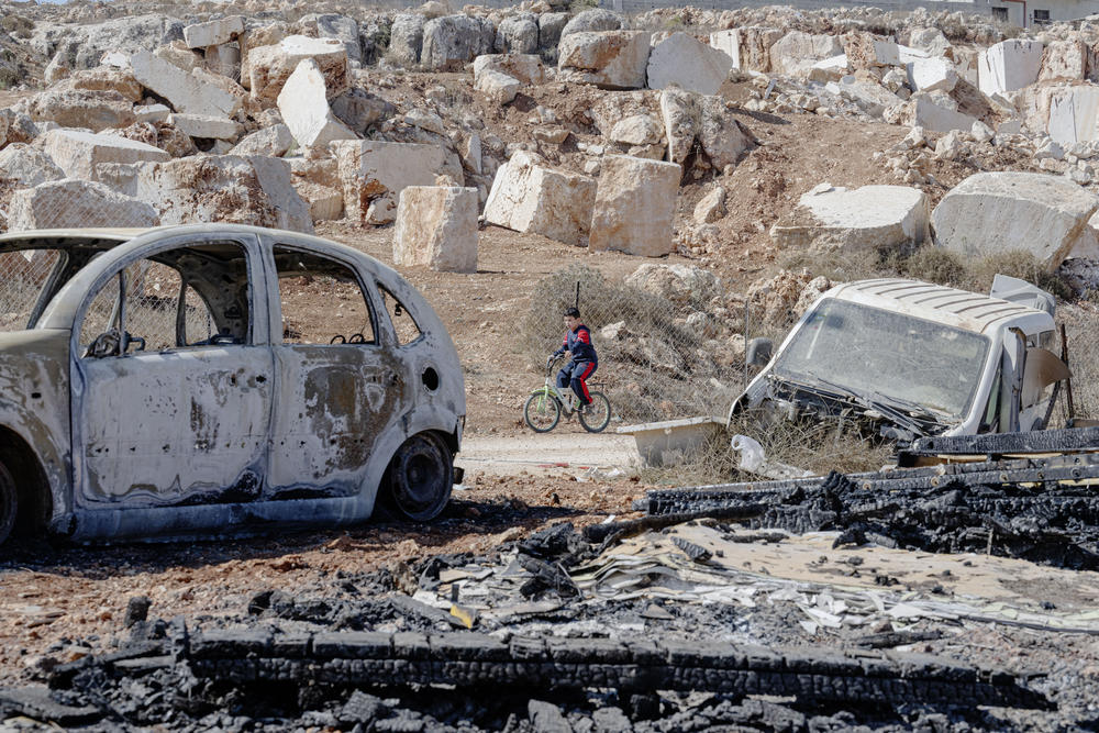 A child rides his bicycle past a torched car in the Palestinian village of Qusra in the occupied West Bank.