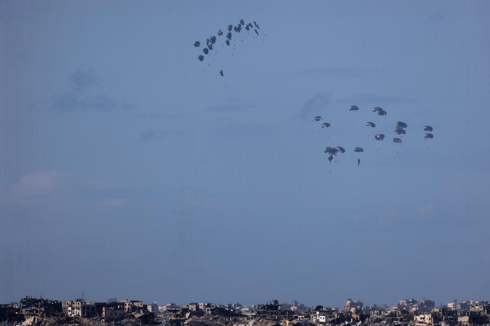 Humanitarian aid falls from planes over northern Gaza as seen from Israel's southern border with the Gaza Strip on March 7, 2024.