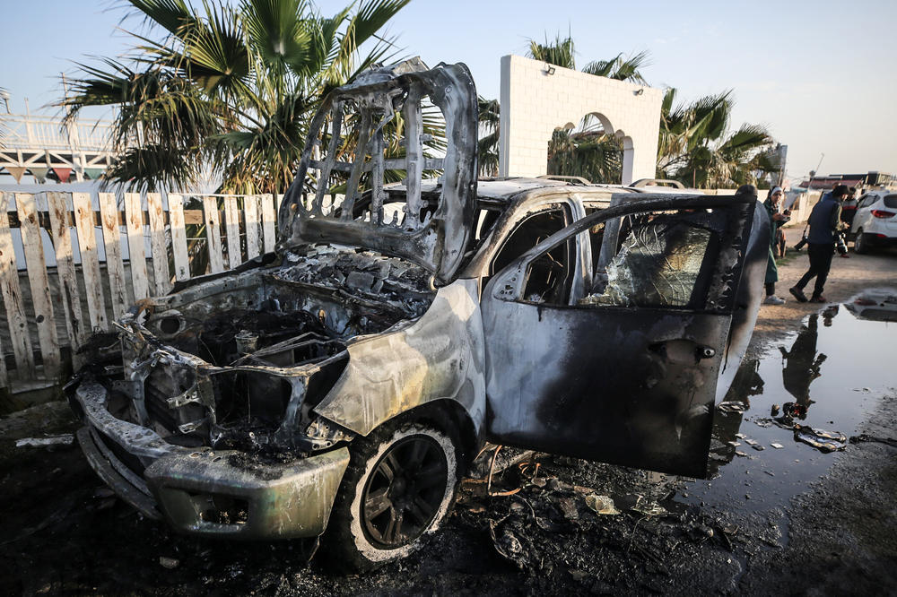 Palestinians are standing next to a vehicle Tuesday in Deir al-Balah, in the central Gaza Strip, where seven aid workers from the World Central Kitchen were killed in an Israeli airstrike.