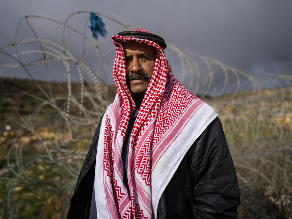 Sakher Abu Dahouk in front of the razor wire of the separation barrier that surrounds his land in Beit Hanina Al-Balad in the Israeli-occupied West Bank. His extended family has moved several times since 1948, as Israel seized territory in subsequent wars, redrew boundaries and built more Jewish settlements. 