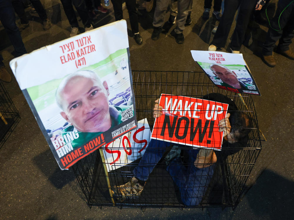 A man sits in a cage with portraits of 47-year-old Israeli hostage Elad Katzir as relatives and supporters of Israeli hostages stage a demonstration in Tel Aviv on March 26.