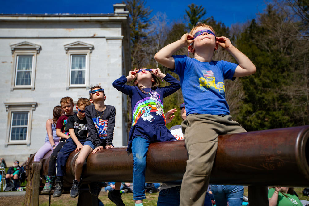 Kids watch the total eclipse begin sitting on a cannon out in front of the Vermont State Montpelier, Vermont on April 8, 2024.