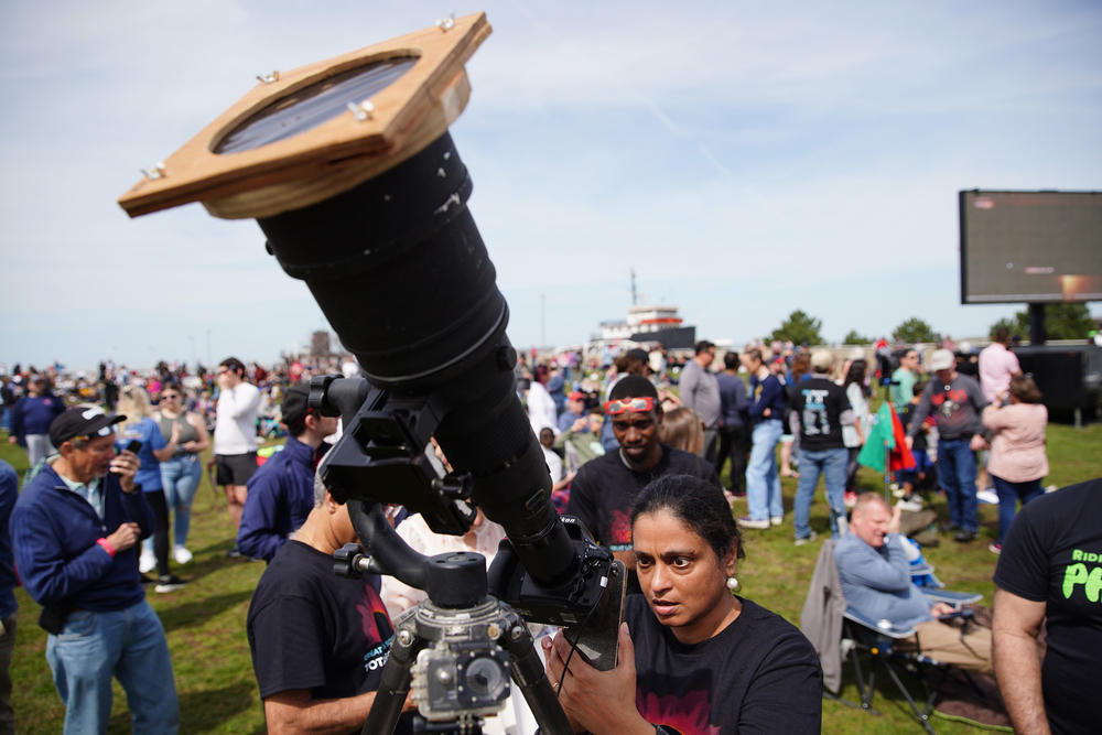 Indira Poovambur, of North Olmsted, Ohio, attempts to take a photo of the sun via the LCD screen of a camera with a telephoto lens outside the Great Lakes Science Center in Cleveland.
