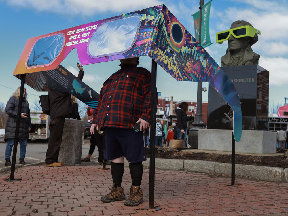 Visitors look through a pair of oversized eclipse glasses set up in the town square on Sunday in Houlton, Maine.