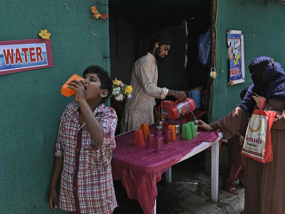 A volunteer distributes drinking water next to a bus stand on a hot summer day in Hyderabad, India, Thursday, March 21, 2024.
