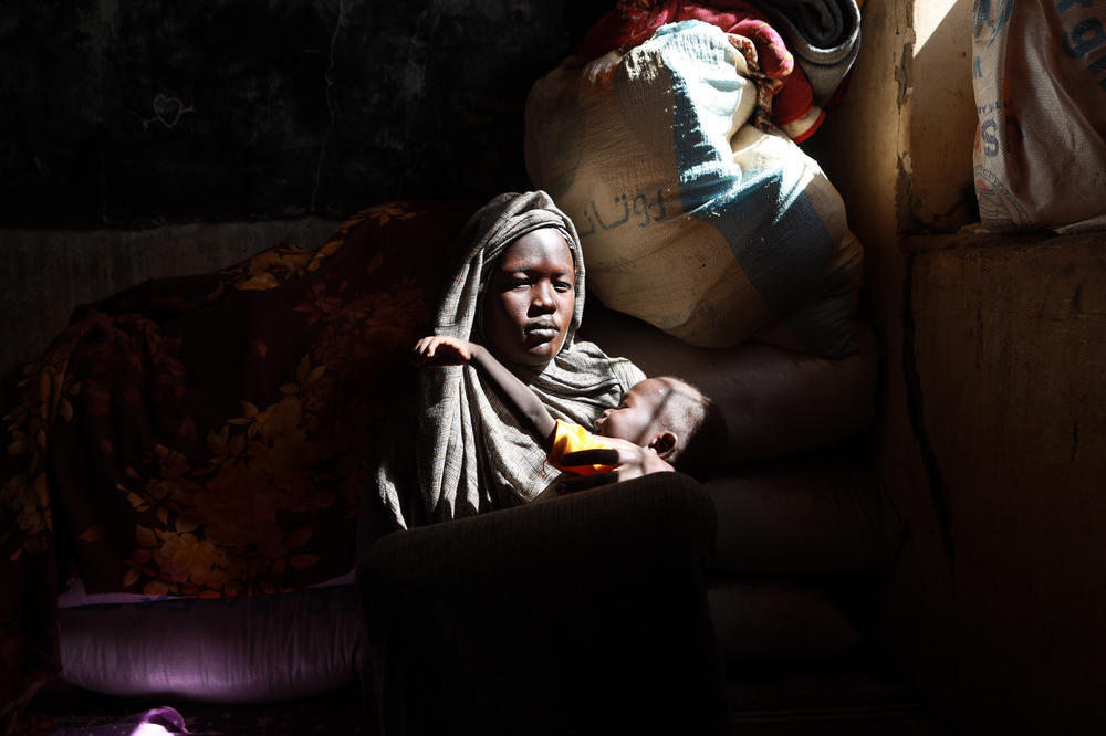 Sarah Dink carries her child while going to a camp in Gezira state, on Dec. 10, 2023. She says, 
