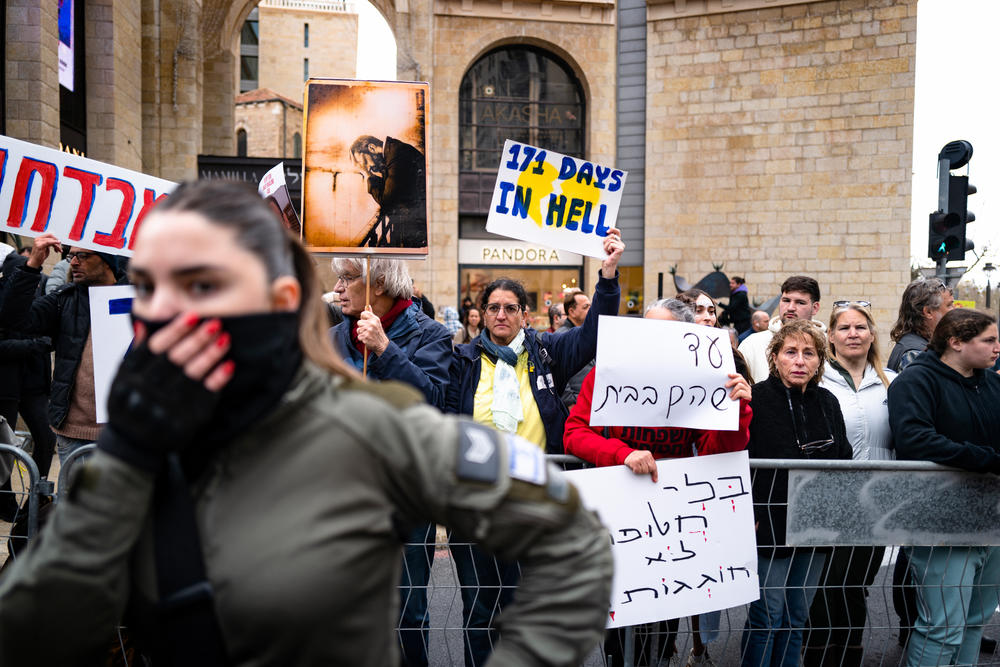 Demonstrators hold signs urging the government to reach a deal for release of hostages taken from Israel by Hamas-led militants on Oct. 7, as they and Israeli security forces watch a parade through Jerusalem for the Jewish holiday of Purim. Despite the war in Gaza, the city hosted an official Purim parade for the first time in more than 40 years, among muted crowds and protesters.