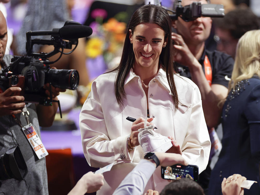 Caitlin Clark, pictured autographing sneakers before the WNBA draft last Monday, is helping drive demand for the league's ticket sales and TV coverage.