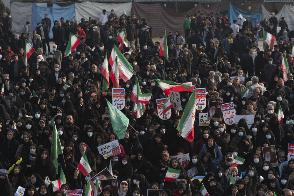 Veiled Iranian women hold Iran flags and placards while attending a pro-government rally in Tehran, in December 2022. The rally was held in opposition to unrest following the death of 22-year-old Mahsa Amini in police custody in September 2022.