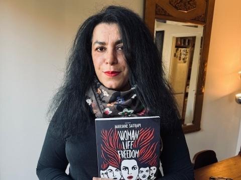 <strong></strong>Marjane Satrapi, a graphic novelist, holds her latest book <em>Woman, Life, Freedom</em>, in her home in Paris, France.