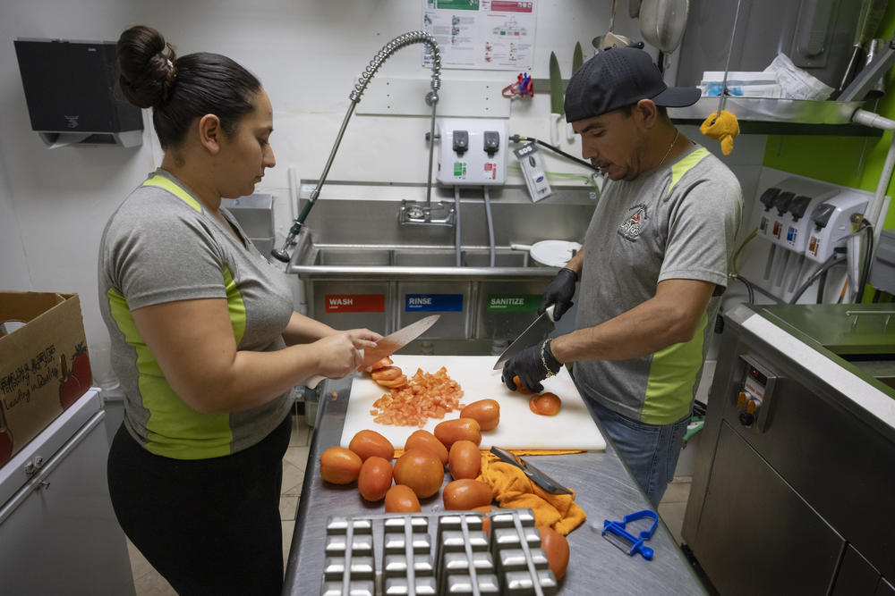 Vazquez, right, and an employee cut tomatoes in the kitchen of his shop.