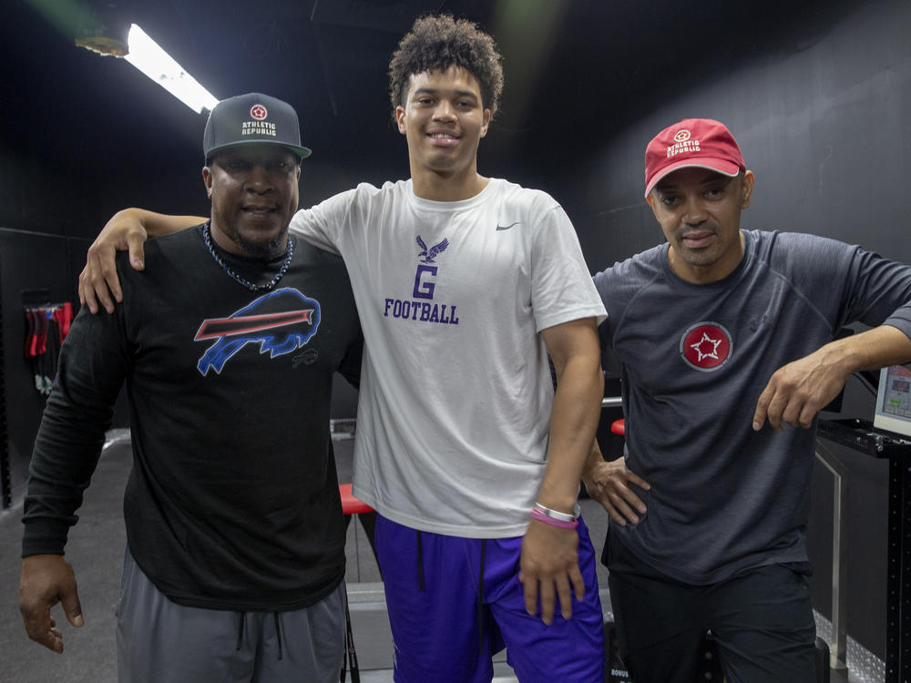 Caleb Williams (C), then a sophomore at Gonzaga College High School, stands with sports performance coach Mark McCain (L) and quarterback trainer Russell Thomas (R) at Athletic Republic in District Heights, Maryland in 2018.