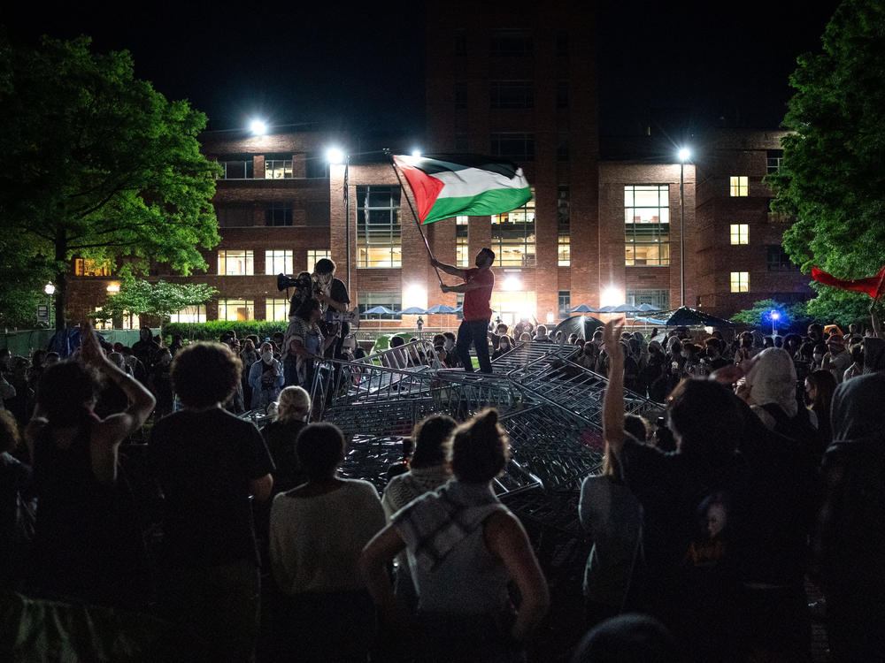 A man holds up a Palestinian flag as activists and students surround piled barricades at an encampment at at George Washington University early Monday.