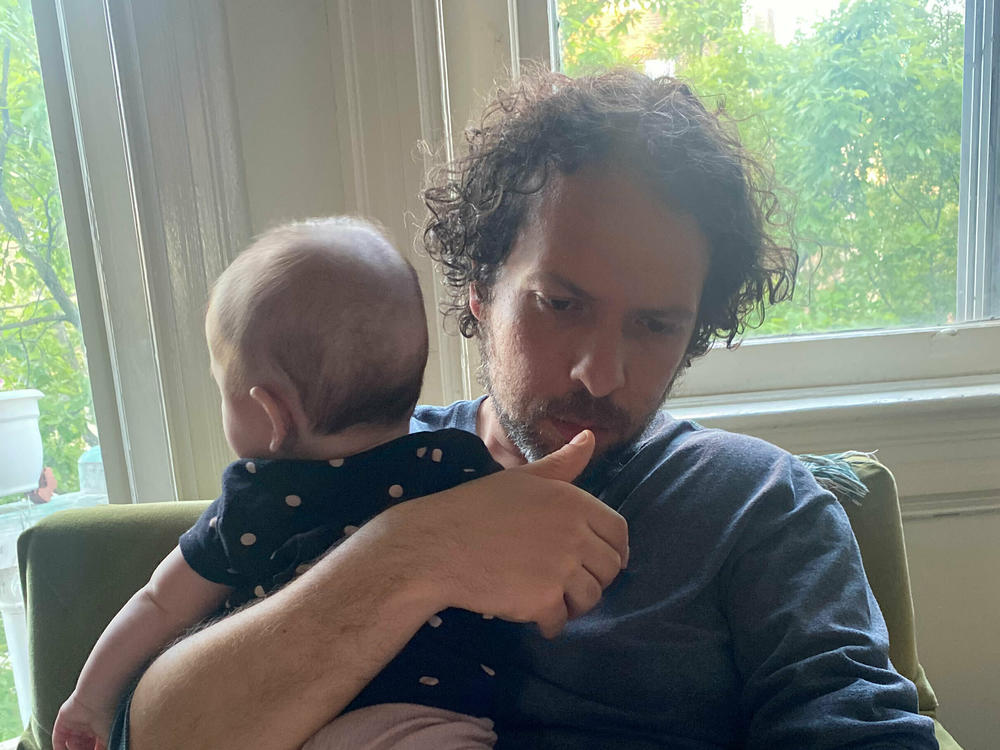 Darius Tahir holds his nearly 5-month-old daughter while puzzling over an instruction manual.