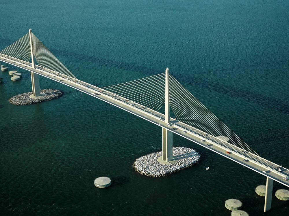 An aerial photo of the Sunshine Skyway Bridge over Tampa Bay in Florida shows both artificial islands surrounding pylons and circular concrete dolphins used as protection against collisions with large vessels.
