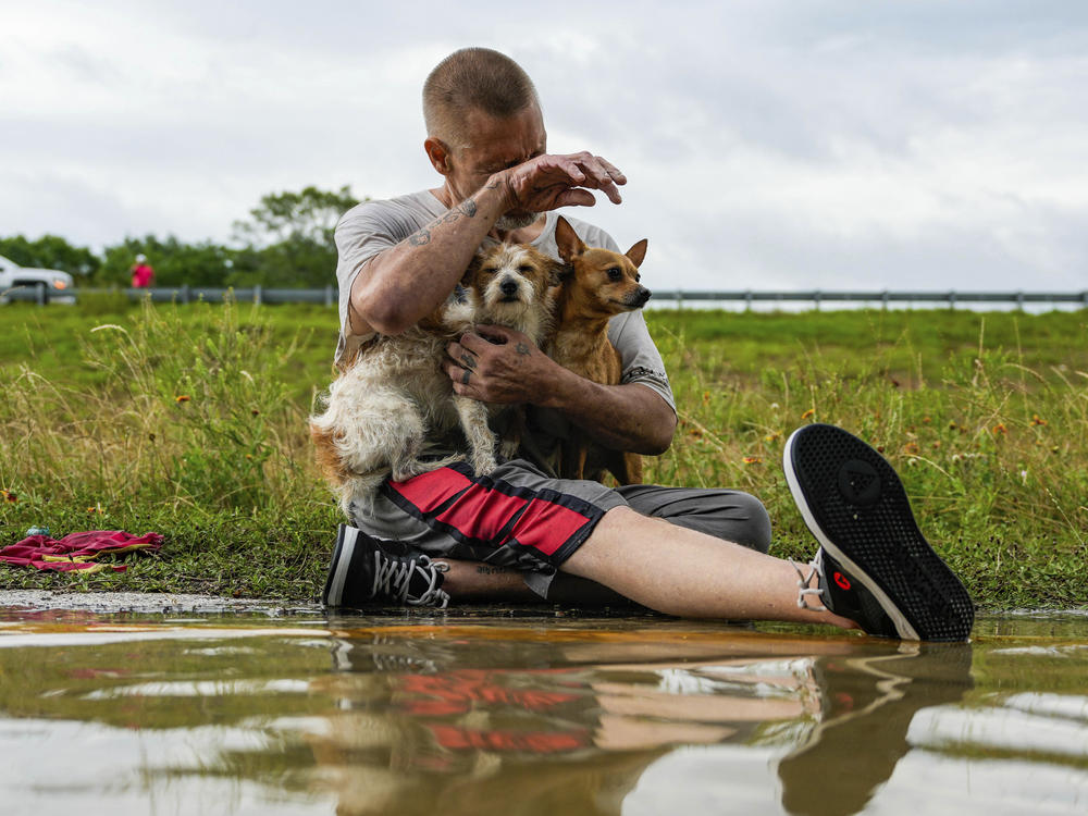 Tim McCanon sits on the road with his dogs after being rescued by the Community Fire Department during severe flooding on Friday in New Caney, Texas.
