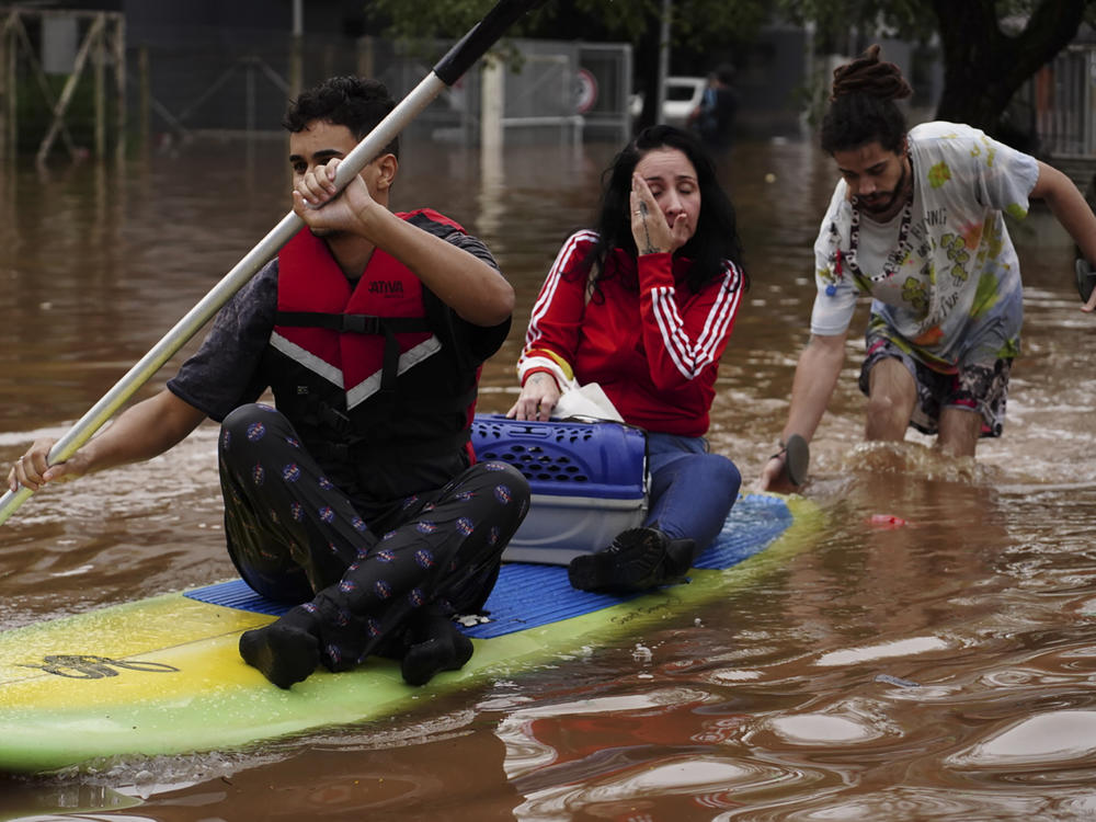 People evacuate on a surfboard from a neighborhood flooded by heavy rains, in Canoas, Rio Grande do Sul state, Brazil, Saturday, May 4, 2024.