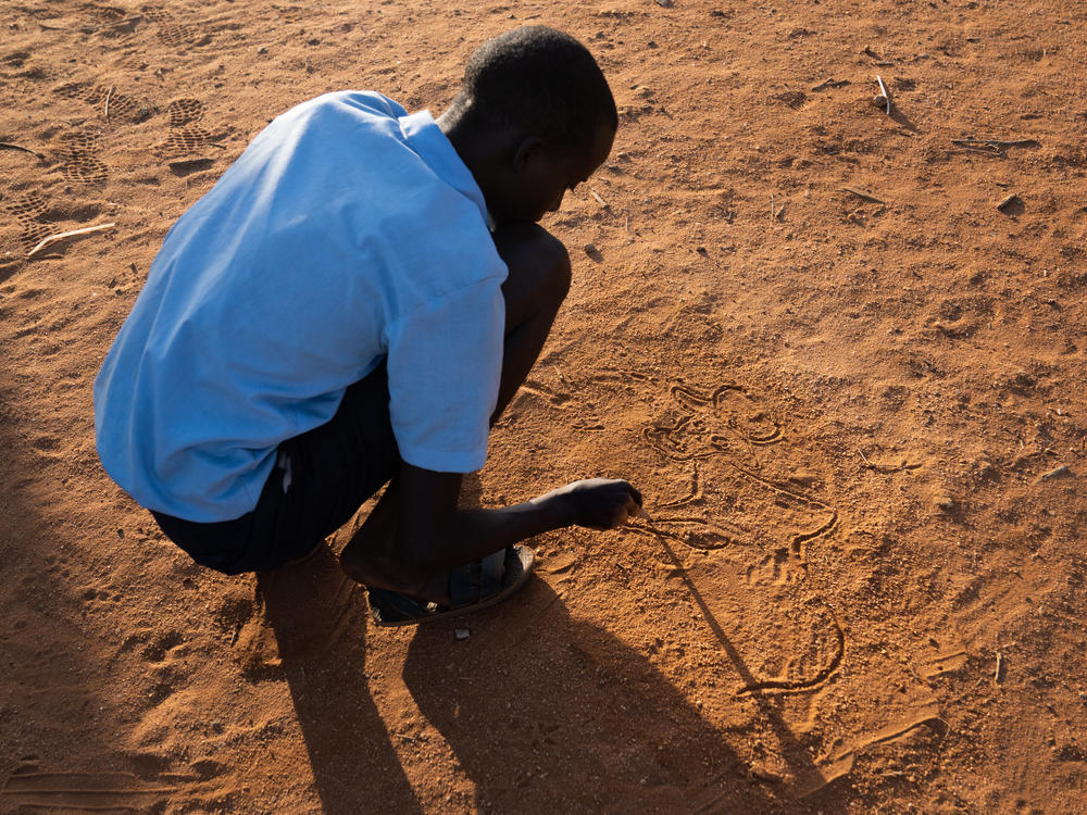 Paris has taught himself to draw. Above, he sketches in the sand at school.