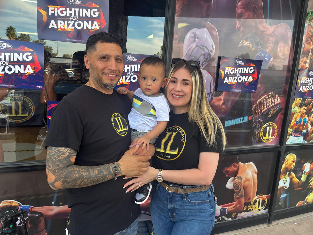 Junior Lopez, owner of JL Boxing Academy in Phoenix, stands outside his business with his wife, Mayrelis Gomez, and their young son.