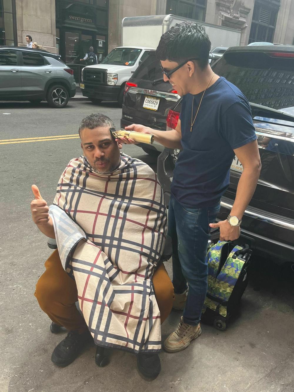 A Venezuelan migrant gets a haircut in the street outside the Roosevelt Hotel, New York's biggest migrant shelter, a block from Grand Central Terminal.