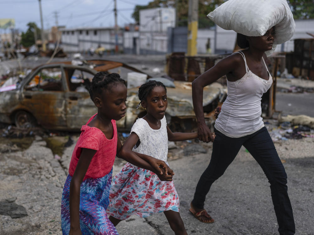 Girls holding hands are led past a burnt car blocking the street as they evacuate the Delmas 22 neighborhood to escape gang violence in Port-au-Prince, Haiti, May 2.